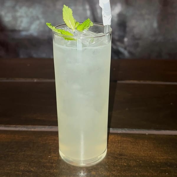 Tall glass of iced lemonade garnished with fresh mint leaves and a straw on a wooden table.