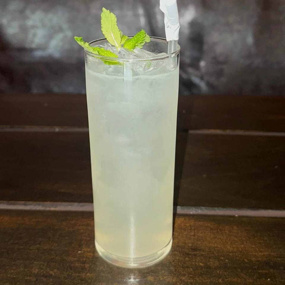 Tall glass of iced lemonade garnished with fresh mint leaves and a straw on a wooden table.