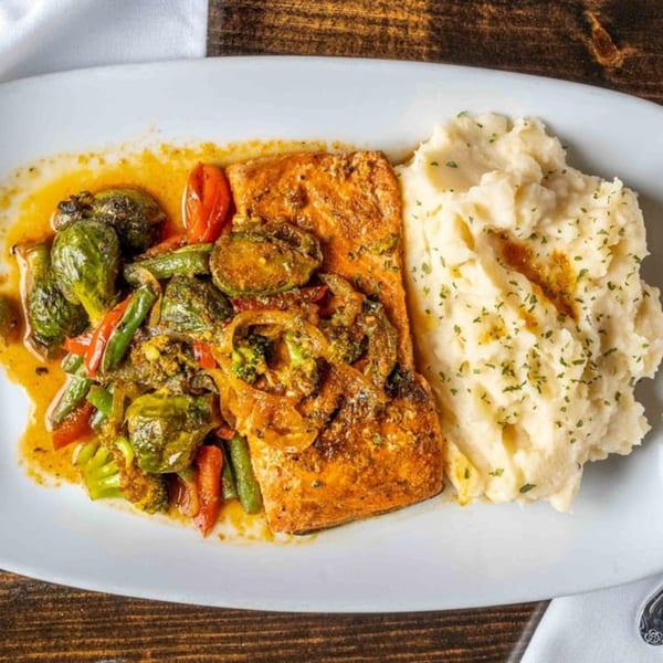 Salmon fillet with roasted vegetables and mashed potatoes on a white plate.