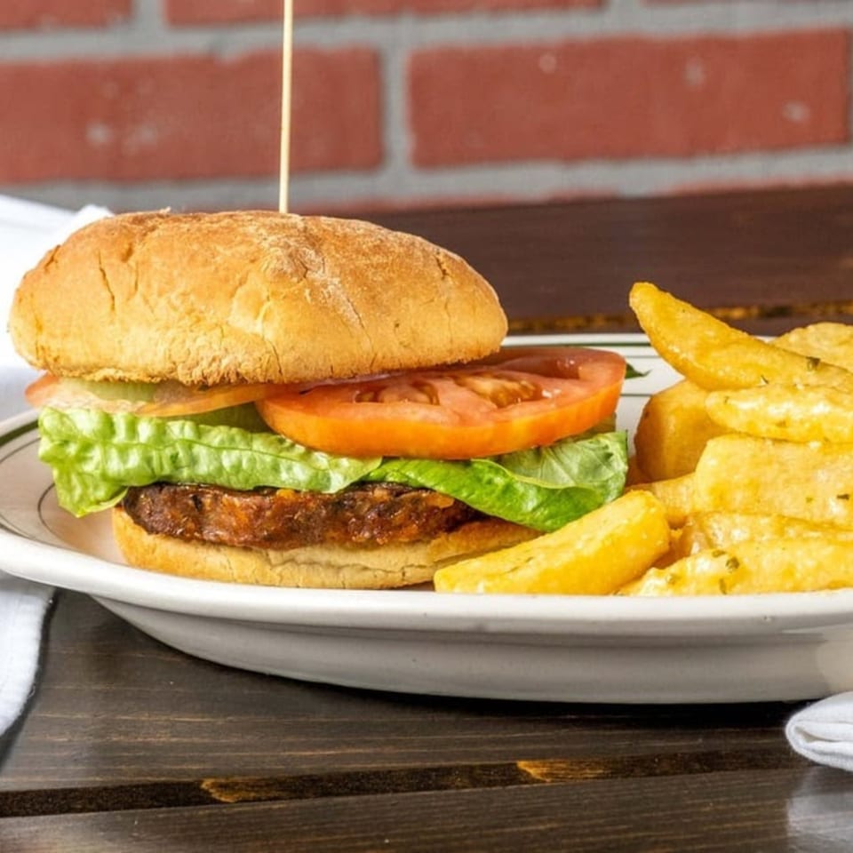 A burger with lettuce and tomato, served with a side of golden french fries on a white plate.