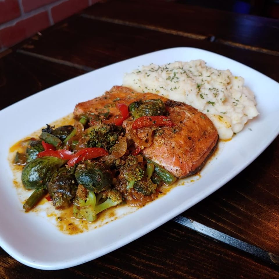 Two salmon fillets with roasted vegetables and mashed potatoes on a white rectangular plate.