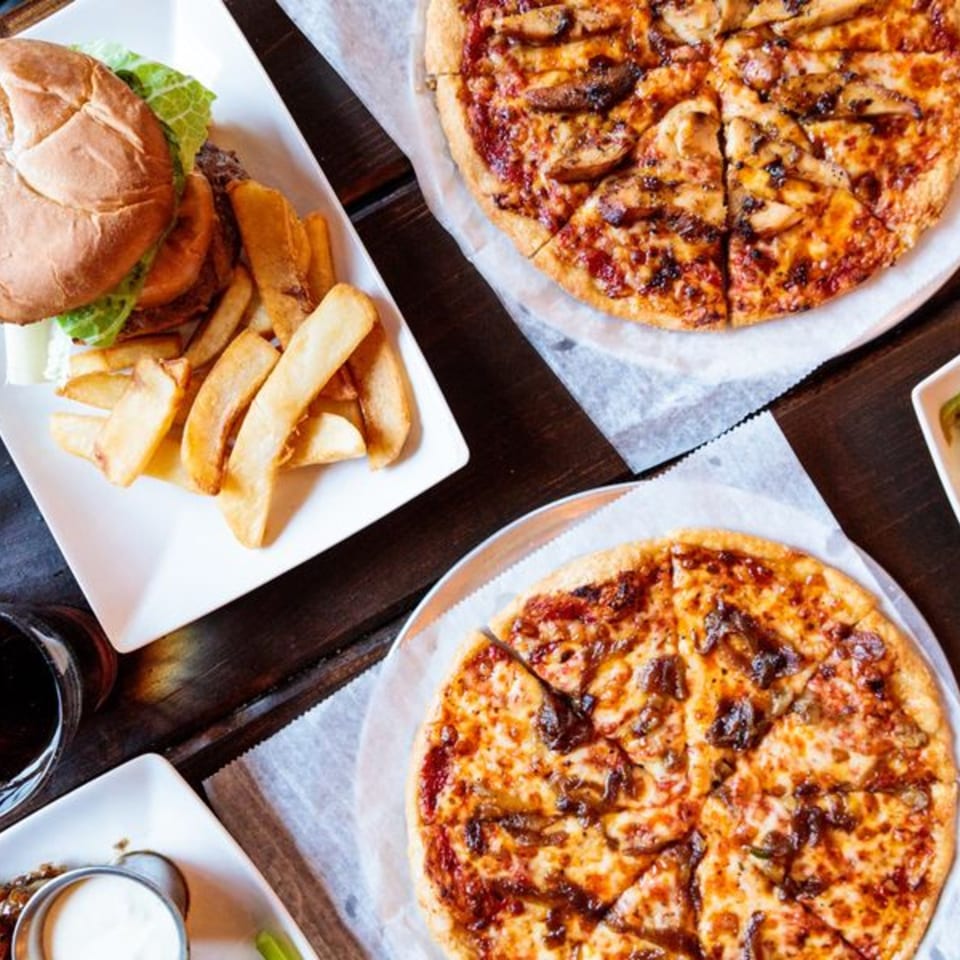 Overhead view of a burger with fries and two pizzas on a rustic wooden table.