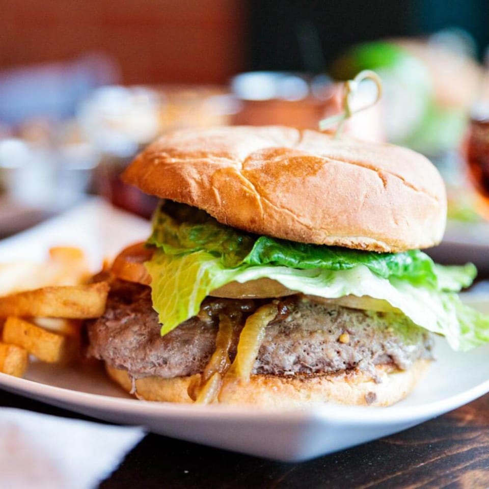 A juicy burger with lettuce, caramelized onions, and a side of fries on a white plate.