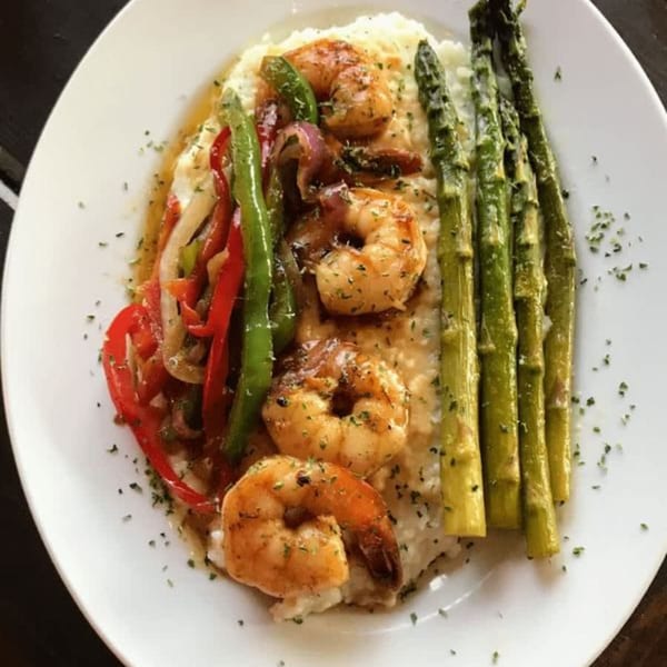 Shrimp and grits with sautéed bell peppers, onions, and asparagus on a white plate.