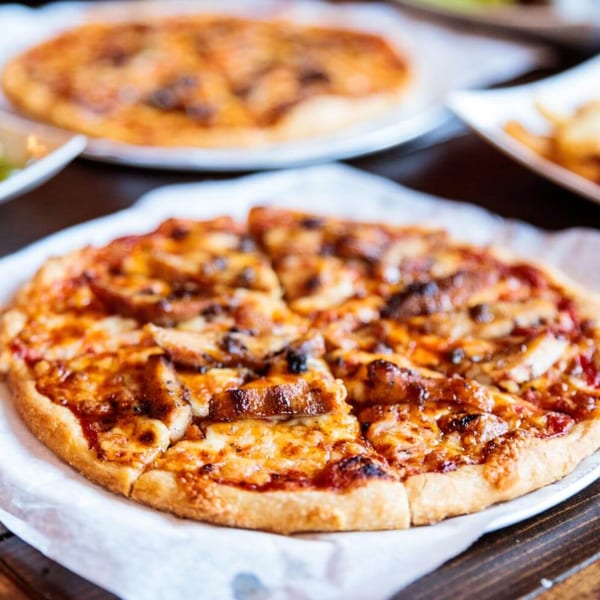 A freshly baked, sliced pizza with melted cheese and toppings on a white paper-lined plate.