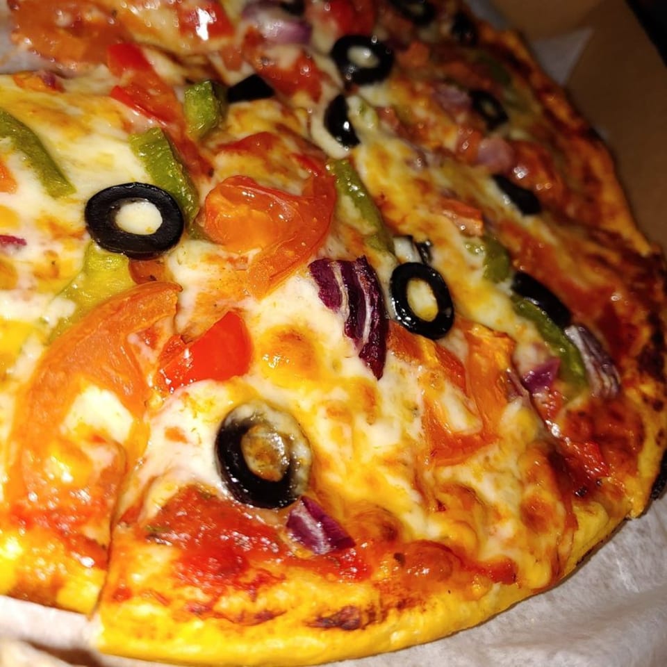 Close-up of a pizza with melted cheese, black olives, red onions, and bell peppers.