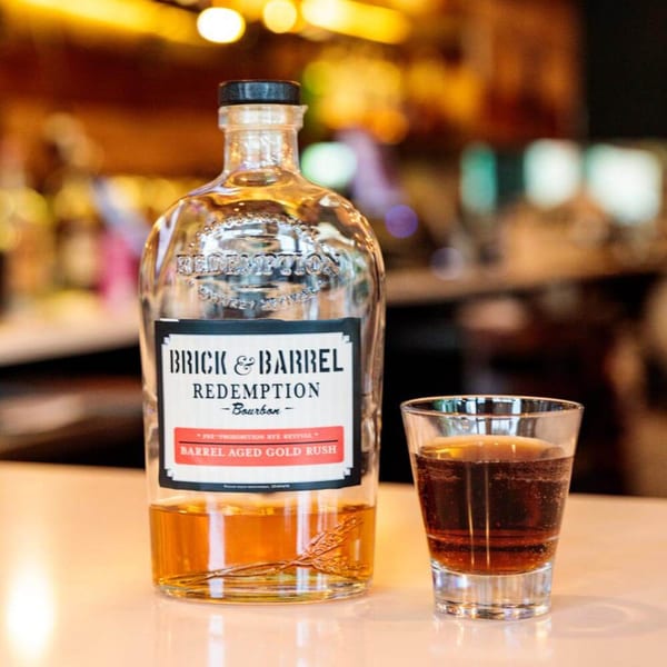 A bottle of Brick & Barrel Redemption Bourbon next to a glass of whiskey on a bar.