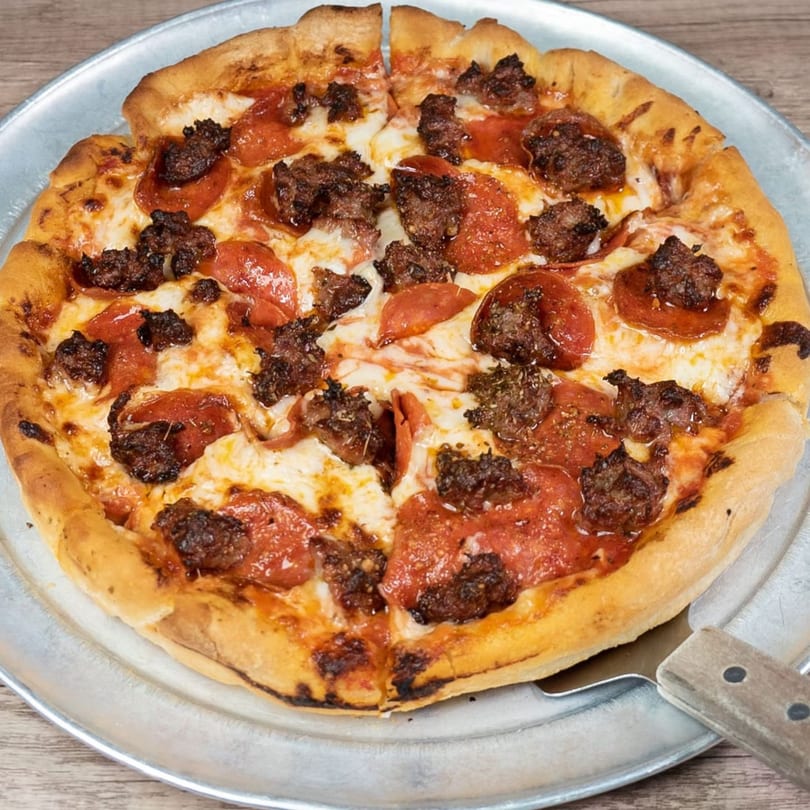 A pepperoni and sausage pizza on a metal pan with a pizza server underneath.