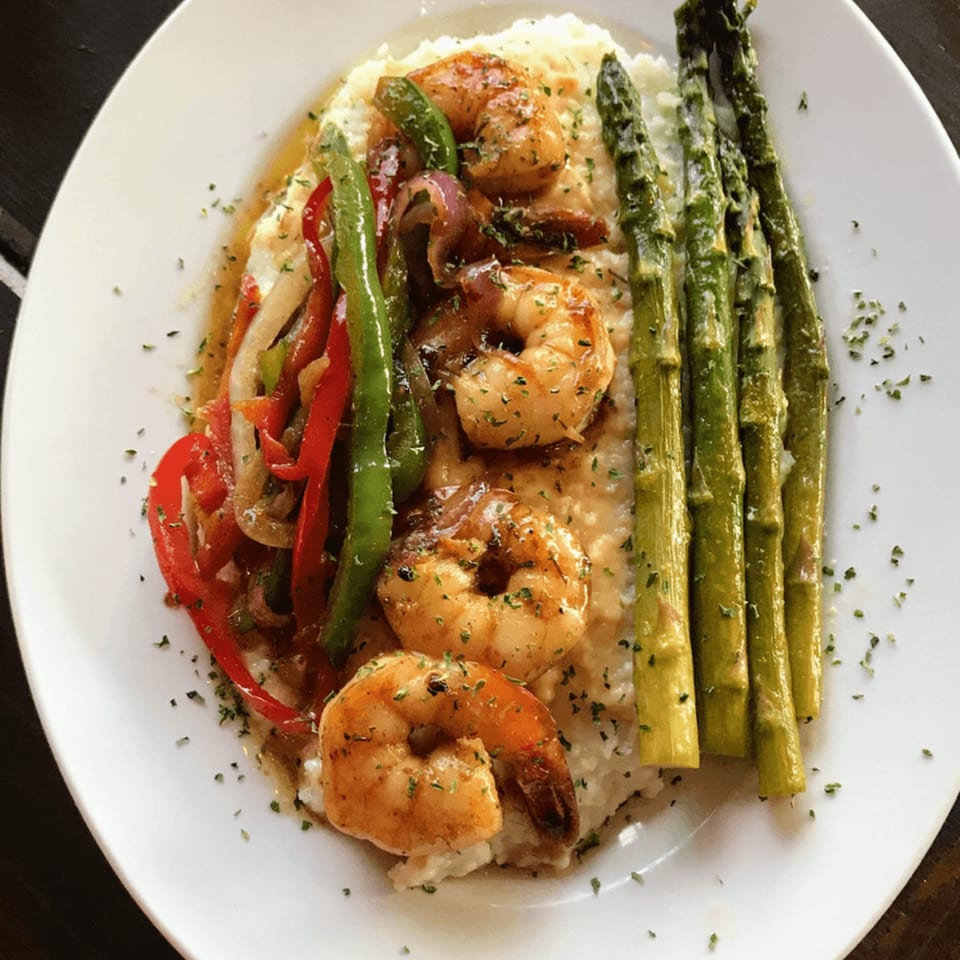 Shrimp and grits with sautéed bell peppers, onions, and asparagus on a white plate.