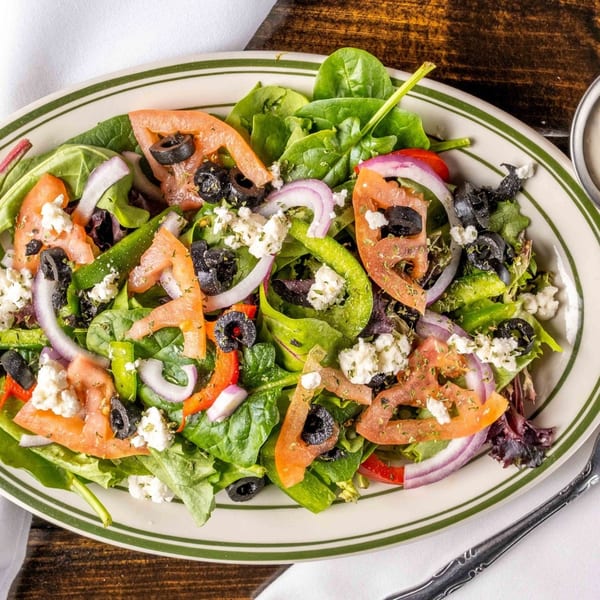 A vibrant salad with spinach, tomatoes, olives, red onion, green peppers, and feta cheese.
