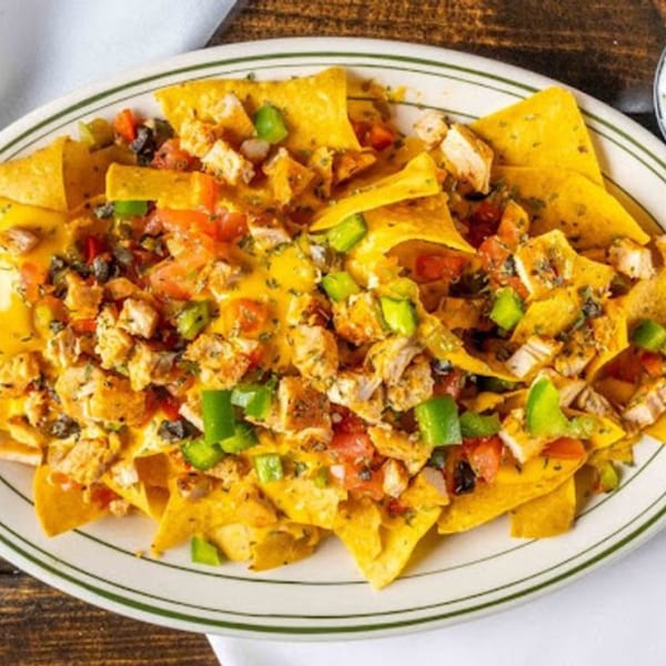 A plate of chicken nachos with melted cheese, diced tomatoes, green peppers, and black olives.